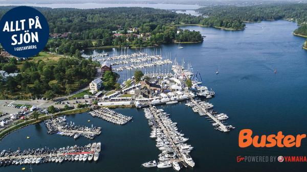 Flygfoto av Gustavsbergs hamn. I det övre vänstra hörnet finns mässans logo, i det nedre högra hörnet Buster-logo.