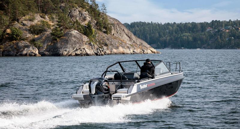 En Buster Magnum VMAX körs nordost på en sjö med en person ombord. I bakgrunden syns en klippa och skogslinjen.